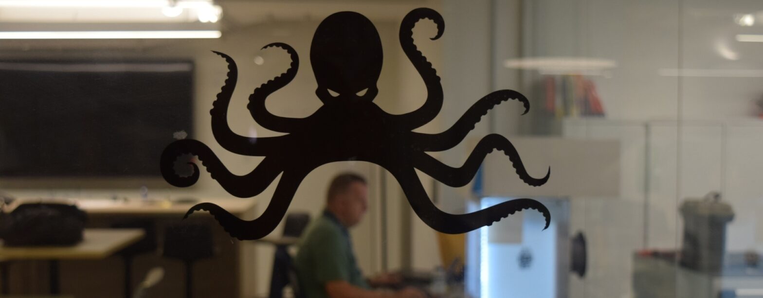 A glass door with a black octopus decal. In the background (blurred behind the glass) is a person working at a computer.